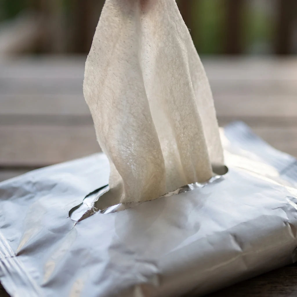 A single wipe pulled halfway out of a foil packet