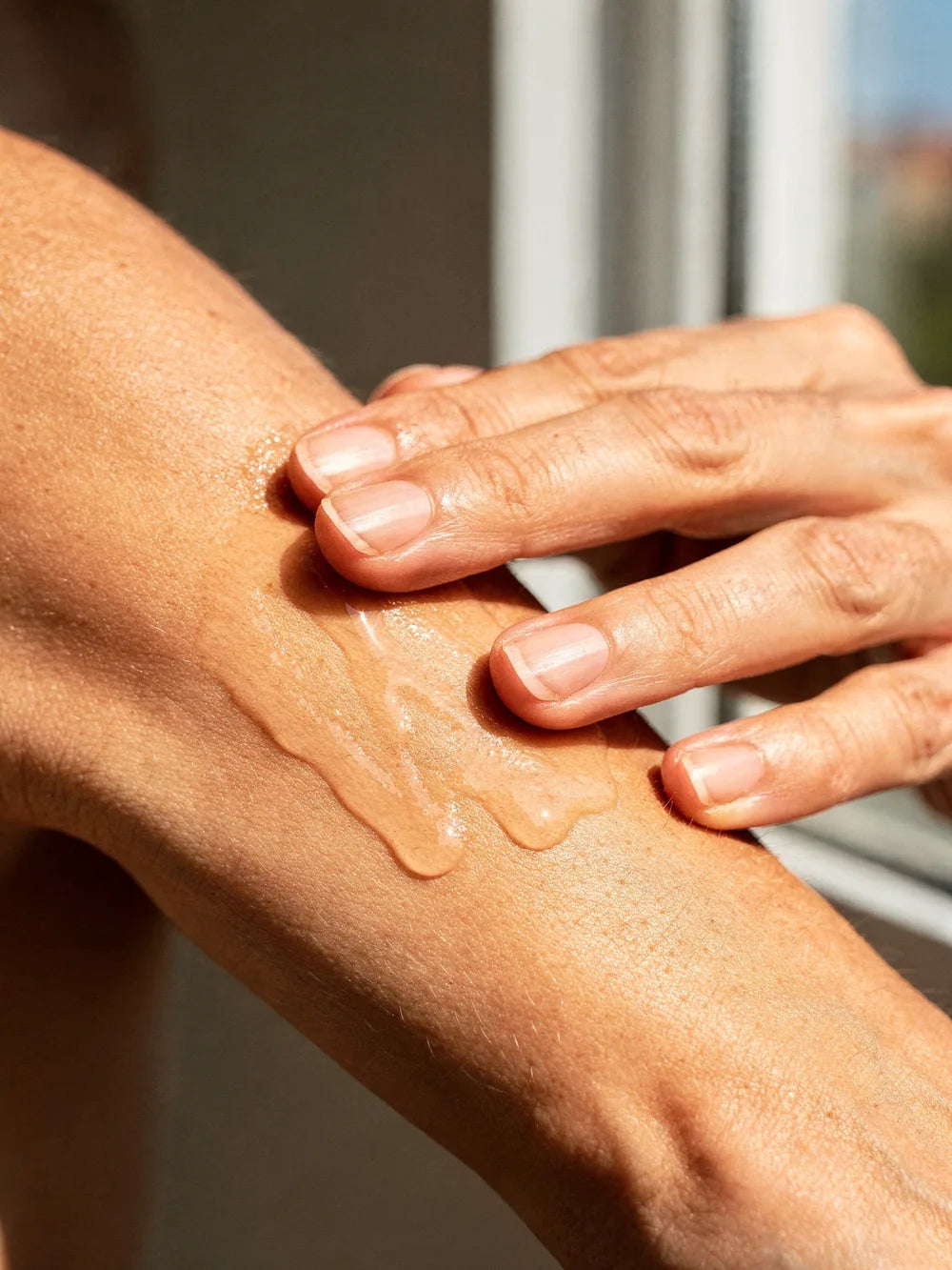 A hand smoothing a drop of oil over a freshly shaved forearm in afternoon light