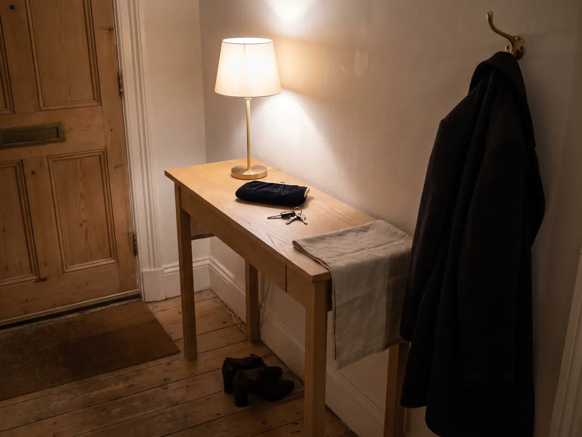A hallway console late at night, a clutch bag and keys set down, shoes stepped out of, the coat back on its hook