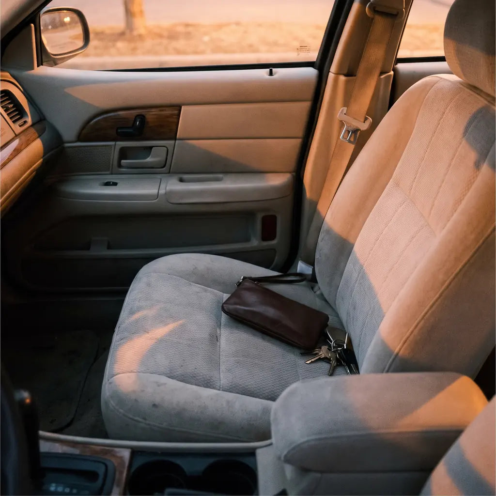 A clutch bag and a set of keys on the passenger seat of a parked car at dusk