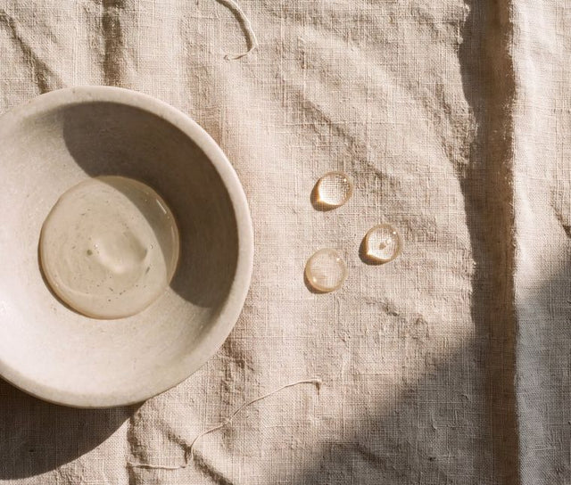 Clear serum in a stone dish, droplets on the linen