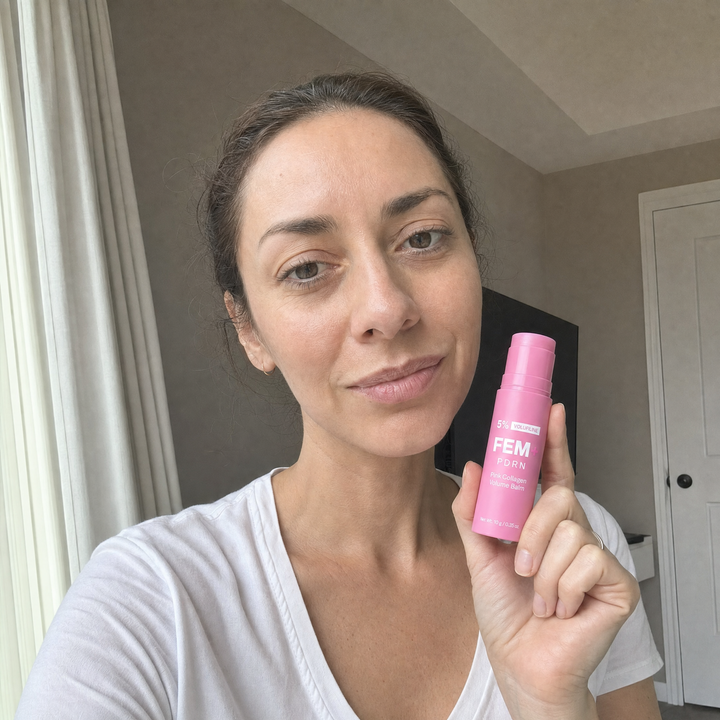 A woman holding the pink FEM+ PDRN stick beside her bare face