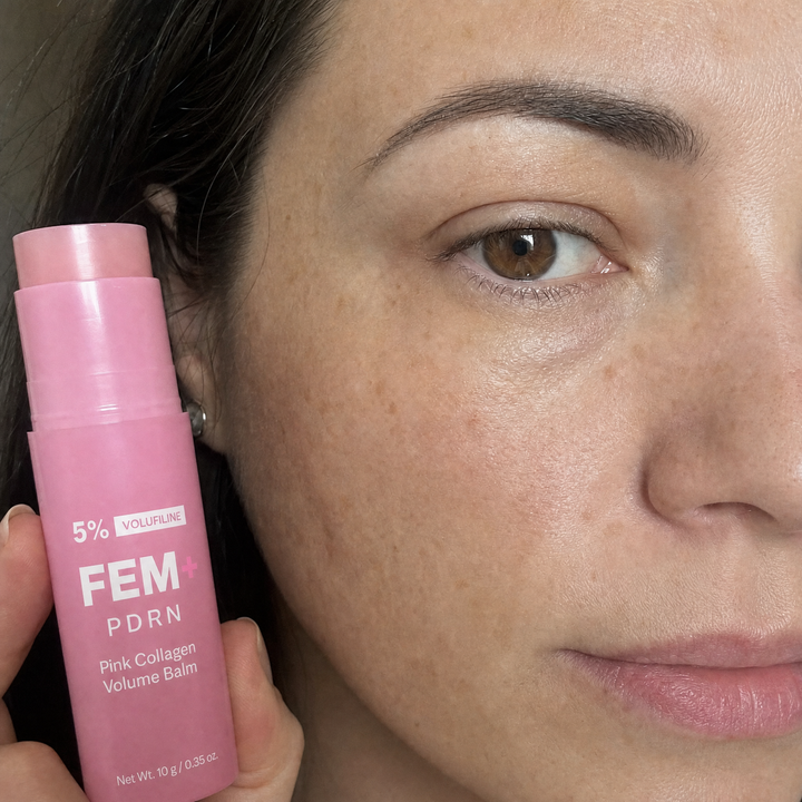 A woman in bed holding the FEM+ PDRN stick, no makeup