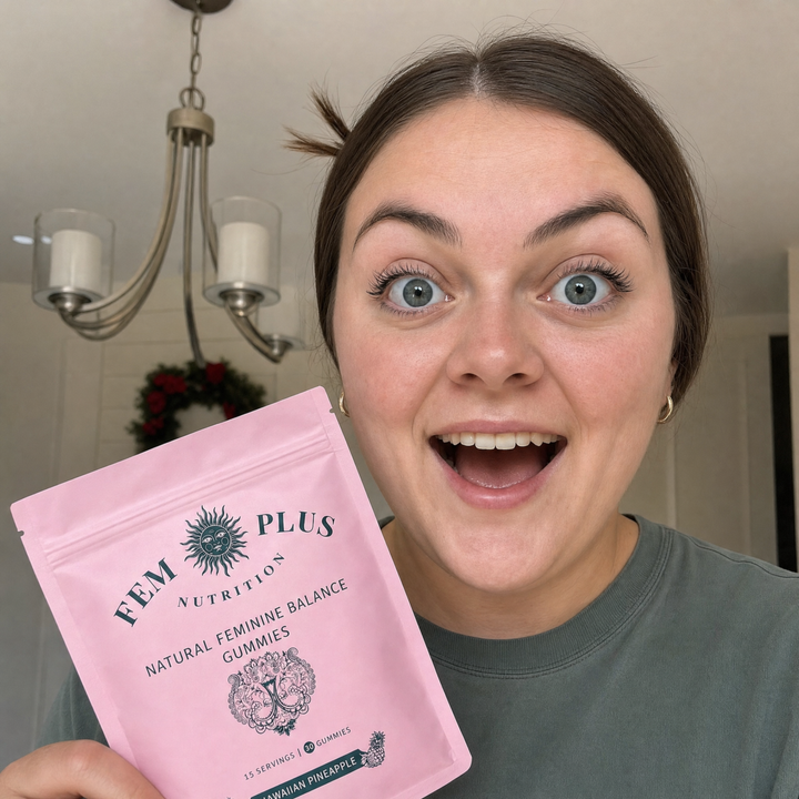 A woman at home holding a pouch of FEM+ gummies beside her face, laughing