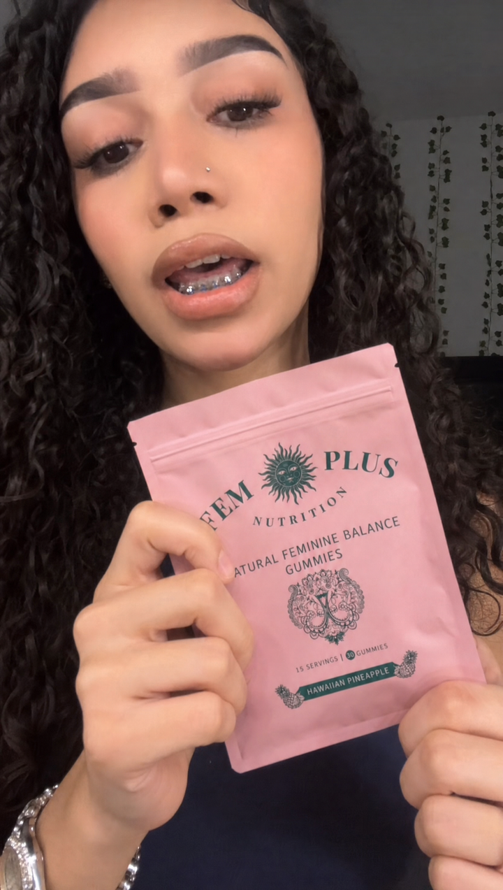 A woman with curly hair holding the FEM+ gummies pouch up beside her
