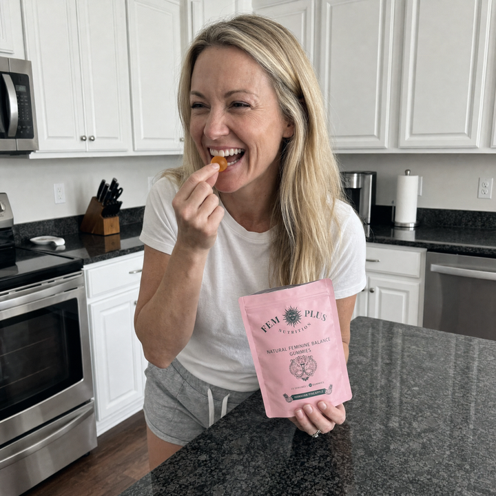 A woman in her kitchen eating a gummy, the pouch open on the counter