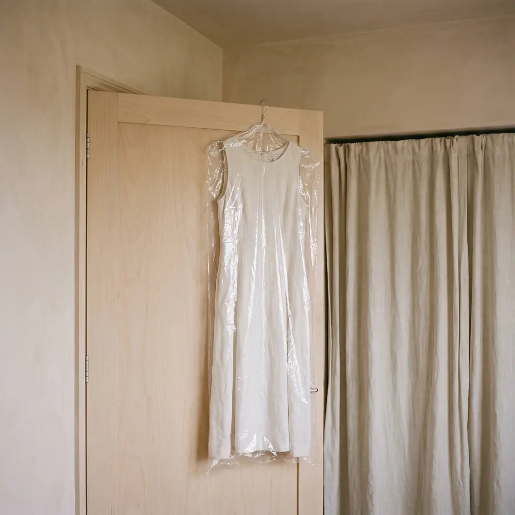A dress still sealed in a dry cleaner’s bag hanging unworn on the back of a bedroom door